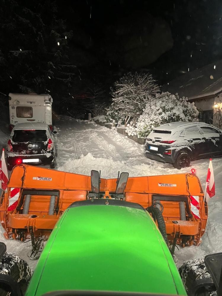 Schneepflug auf der Straße mit parkenden Autos im Weg