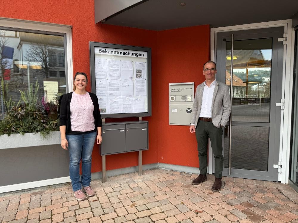 Hauptamtsleiterin Jennifer Hopf und Bürgermeister Jörg Frey vor dem neuen Briefkasten mit Bekanntmachungstafel am Schonacher Rathaus