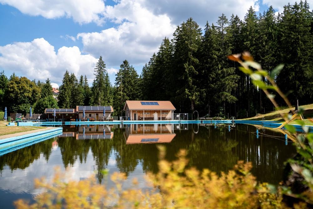 Naturschwimmbad mit Wasserfläche und Kioskgebäude im Hintergrund Naturschwimmbad mit Wasserfläche und Kioskgebäude im Hintergrund